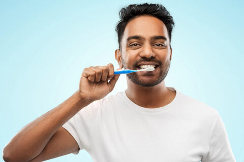 Portrait of a man brushing his tooth with a smile wearing white tshirt